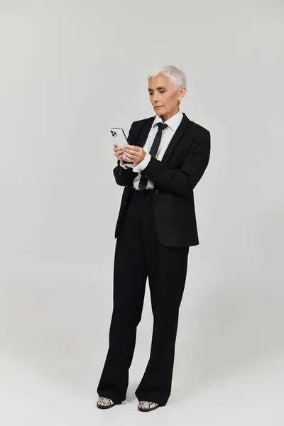 Mature woman with short hair checks her smartphone, exuding confidence and style. — Stock Photo