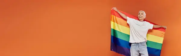 A mature woman radiates joy while holding a vibrant rainbow flag. — Stock Photo