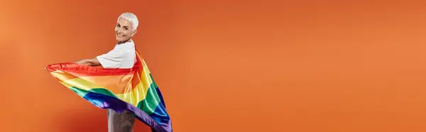 Mature woman joyfully wraps herself in a rainbow flag, embracing her identity with pride. — Stock Photo