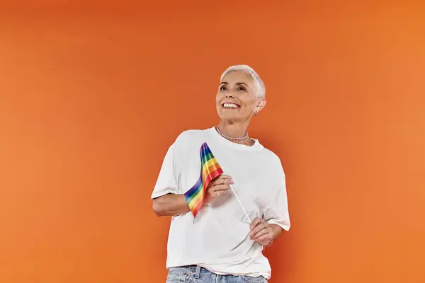 Una donna gioiosa tiene una bandiera arcobaleno, irradiando orgoglio e fiducia nel suo vestito elegante. — Foto stock