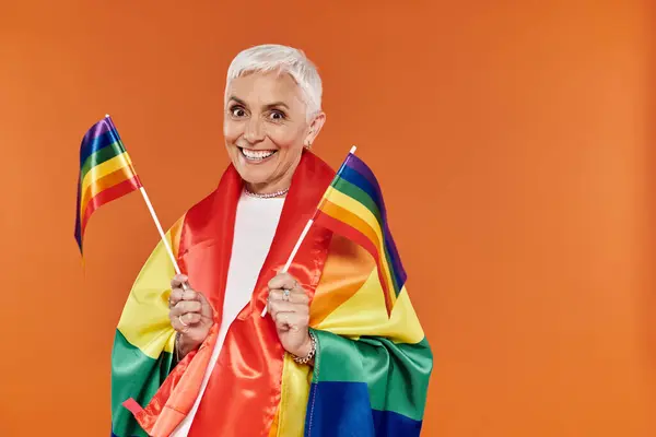 A vibrant celebration with a smiling mature lesbian waving rainbow flags. — Stock Photo