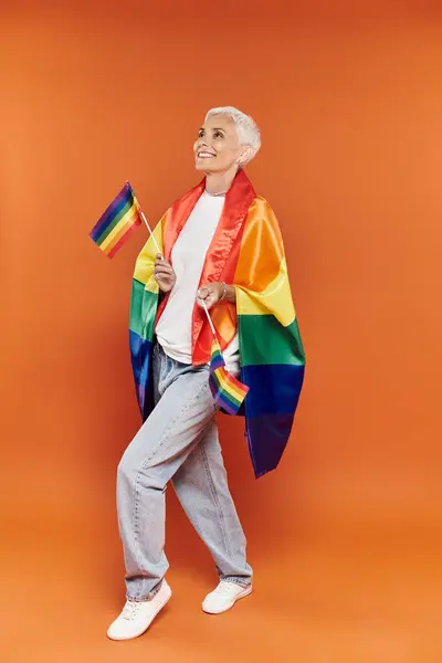 Eine reife, stilvolle Frau umarmt freudig ihre Identität mit Regenbogenfahnen. — Stockfoto