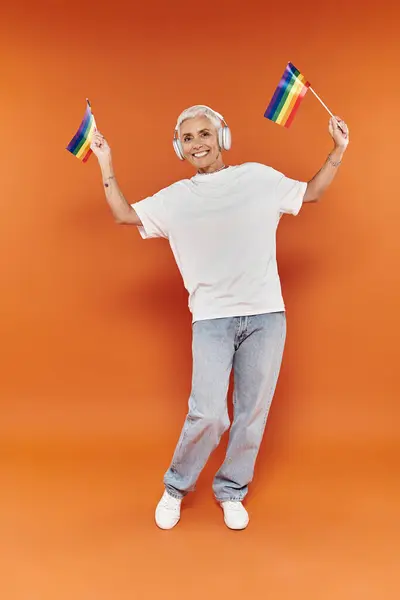 A stylish woman dances with rainbow flags, radiating happiness and pride. — Stock Photo