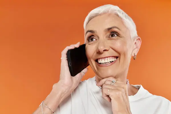 Una mujer madura con el pelo corto felizmente chats en su teléfono, irradiando alegría. - foto de stock