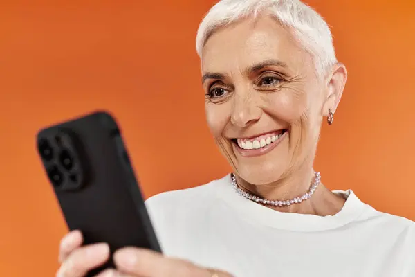 Mature woman enjoying a moment while looking at her phone, exuding joy and style. — Stock Photo