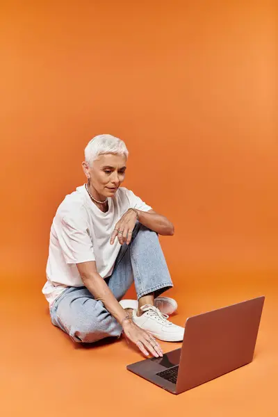 Mature woman with short hair interacts with a laptop in a vibrant setting. — Stock Photo