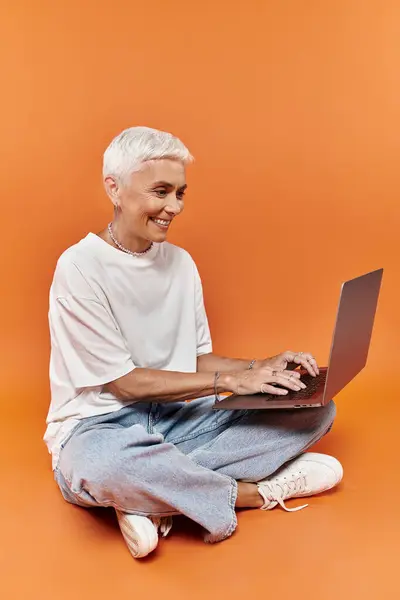 A mature woman with short hair smiles while using her laptop. — Stock Photo