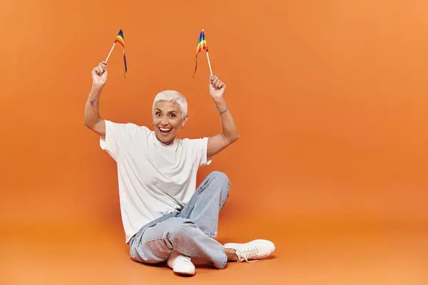 La persona expresa felicidad mientras sostiene banderas de arco iris en una atmósfera brillante. - foto de stock