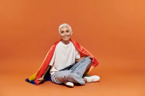 Mujer madura irradia alegría mientras está sentada, envuelta en una capa de orgullo colorido. - foto de stock
