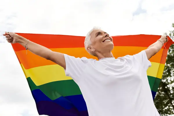 Una mujer confiada levanta alegremente una bandera del arco iris, abrazando su identidad y comunidad. - foto de stock