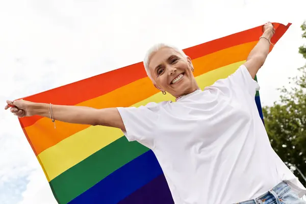 A joyful presence embraces a vibrant rainbow flag against a bright sky. — Stock Photo