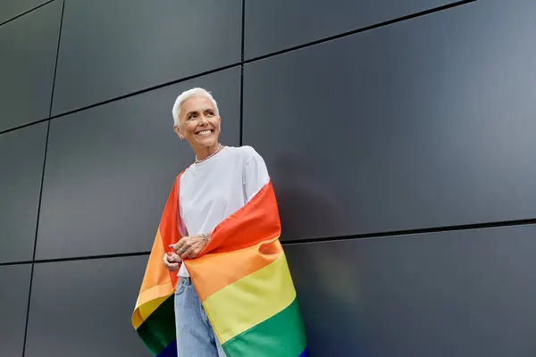 Eine selbstbewusste Frau in eine Regenbogenfahne gehüllt lächelt in einer städtischen Umgebung. — Stockfoto