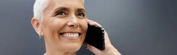 Una mujer madura sonríe brillantemente mientras habla por teléfono. - foto de stock