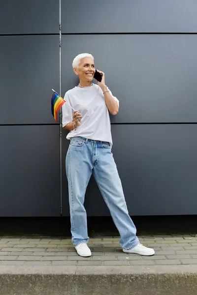 A joyful woman embraces Pride with a rainbow flag while on a call. — Stock Photo