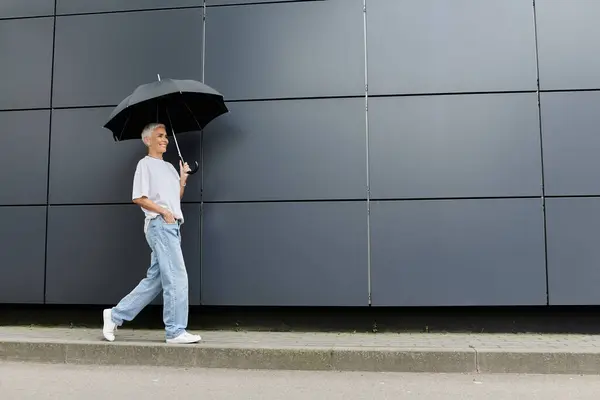 Elegant woman walks confidently with an umbrella on a rainy urban street. — Stock Photo