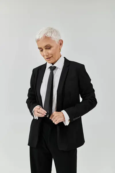 A fashionable woman with short hair adjusts her tie with poise. — Stock Photo