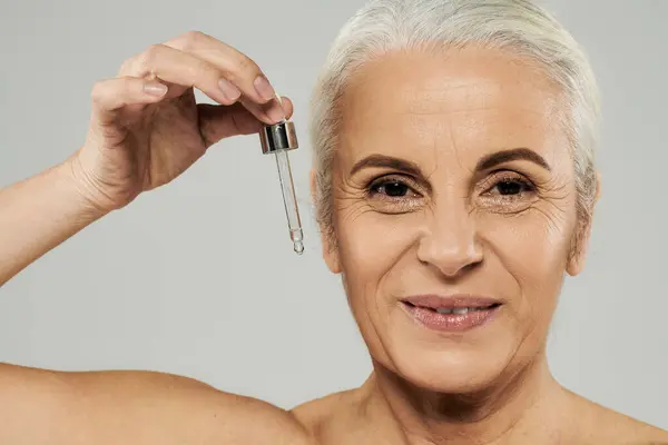 A mature woman using serum and smiling at camera. — Stock Photo