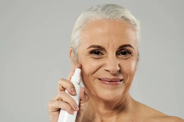 A mature woman smiles while applying skincare. — Stock Photo