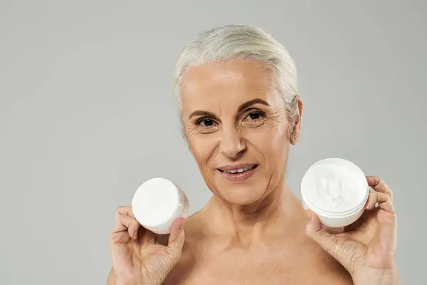 A mature woman holding skincare products. — Stock Photo