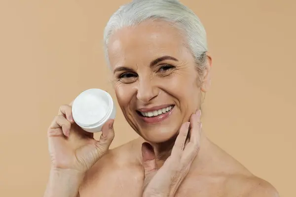 A mature woman smiling joyfully and holding cream jar. — Stock Photo