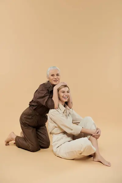 Una mujer madura y su hija adulta comparten un abrazo alegre en un ambiente de tonos suaves. - foto de stock