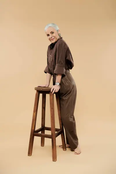 A mature woman leans gracefully on a wooden stool, exuding warmth and joy. — Stock Photo
