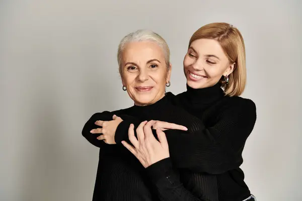A mature woman smiles while her daughter embraces her warmly from behind. — Stock Photo