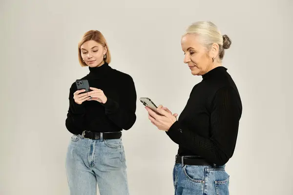 A mature woman and her adult daughter focused on their smartphones together. — Stock Photo