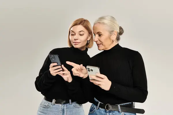 A mother and daughter share a joyful moment while looking at their phones. — Stock Photo