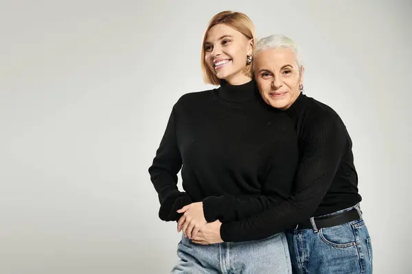 A mother embraces her daughter, both smiling warmly and dressed alike. — Stock Photo