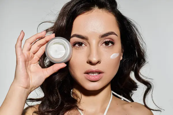 A young woman applies skincare cream while smiling at the lively backdrop. — Stock Photo