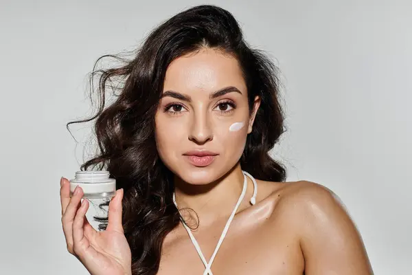 A young woman applies cream while posing against a colorful background. — Stock Photo