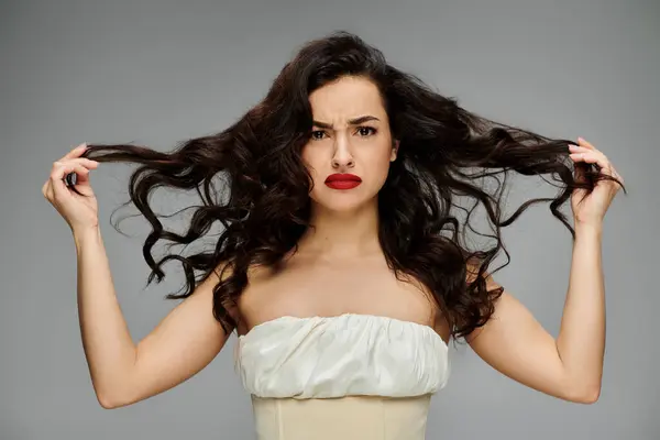 Long haired woman poses gracefully on gray backdrop. — Stock Photo