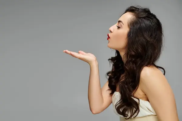 Elegante donna posa con grazia su sfondo grigio, invia un bacio giocoso. — Foto stock