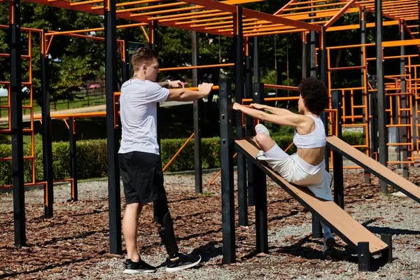 A young woman and a tattooed man with prosthetic leg workout side by side, showcasing strength and friendship in the park. — Stock Photo