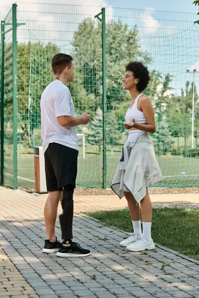 Zwei Freundinnen unterhalten sich vor dem Training in einem Outdoor-Park, zeigen Inklusivität und Freundschaft, ein Mann mit Beinprothese schaut eine Afroamerikanerin an — Stockfoto