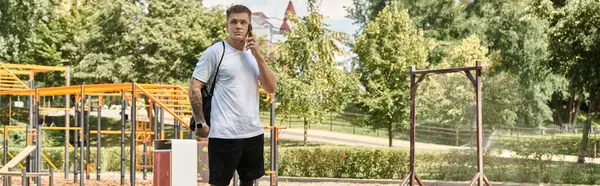 A young man with tattoos walks through a park, talking on his phone — Stock Photo