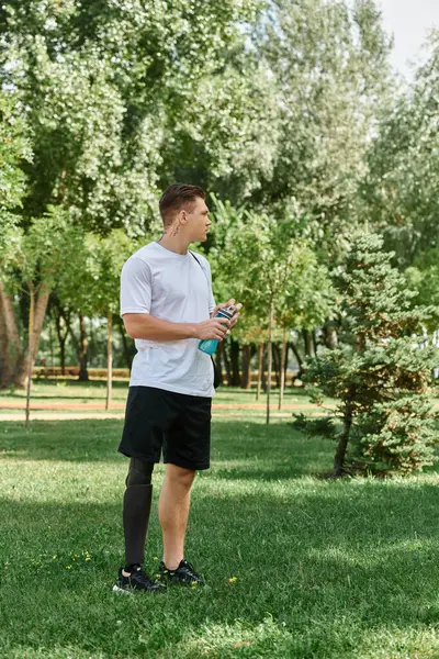 A young man with tattoos sips water in a lush green park, embracing inclusion and outdoor adventure. — Stock Photo