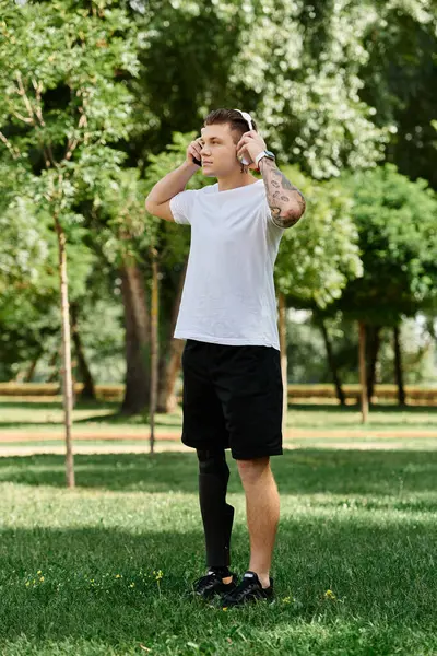 Joven tatuado con pierna artificial disfrutando de la naturaleza y la música en un parque soleado - foto de stock