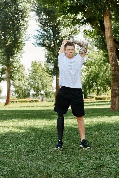 Tattooed young man with prosthetic leg stretching outdoors in a park during the day — Stock Photo