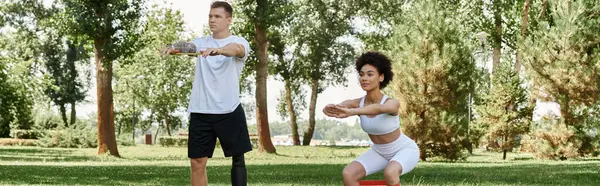 A young woman and tattooed man with a prosthetic leg exercise together in a sunny park. — Stock Photo