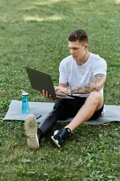 Jovem tatuado com perna protética usando laptop e sentado em esteira de fitness, nômade digital — Fotografia de Stock