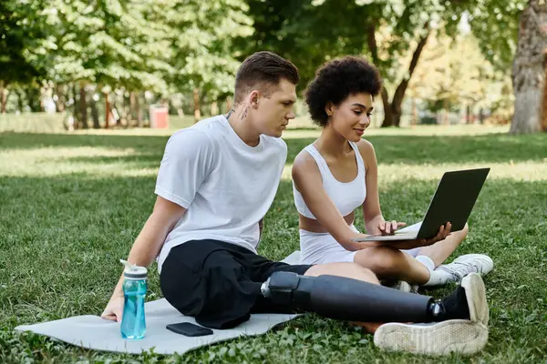 Dos amigos colaboran al aire libre, utilizando el ordenador portátil en el parque - foto de stock