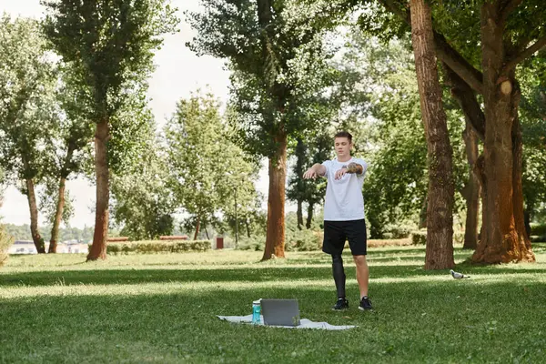 Tattooed young man with artificial leg working out in green park, engaging in an online fitness lesson — Stock Photo