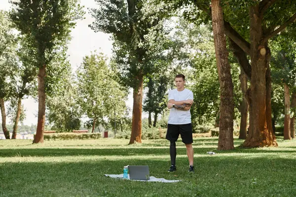 Tattooed man with artificial leg working out in green park, engaging in an online fitness lesson — Stock Photo
