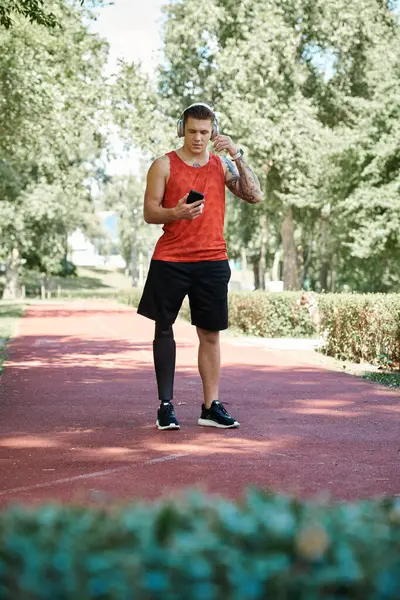 Um jovem tatuado na perna protética usando melodias de desgaste ativo em sua rotina de exercícios ao ar livre — Fotografia de Stock