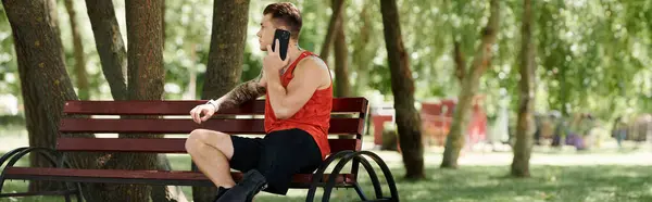 A young man with tattoos sits on a bench in green park outdoors, phone call — Stock Photo