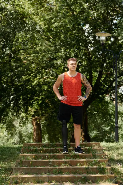 A young man with tattoos stands proudly on steps, training outdoors surrounded by greenery. — Stock Photo