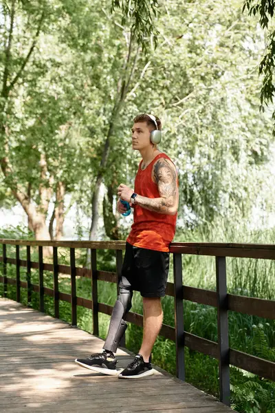 A young man with tattoos and prosthetic leg stands on bridge, with water bottle — Stock Photo