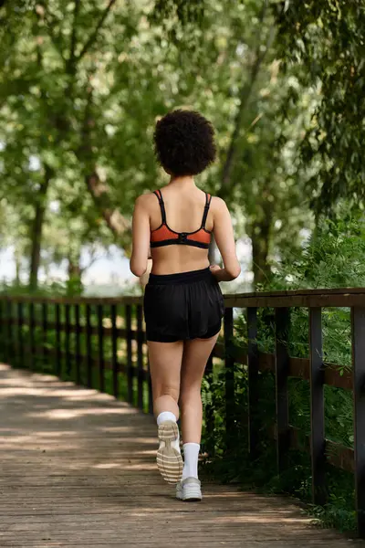 Uma mulher correndo em uma ponte, cercada por árvores vibrantes e ar fresco. — Fotografia de Stock